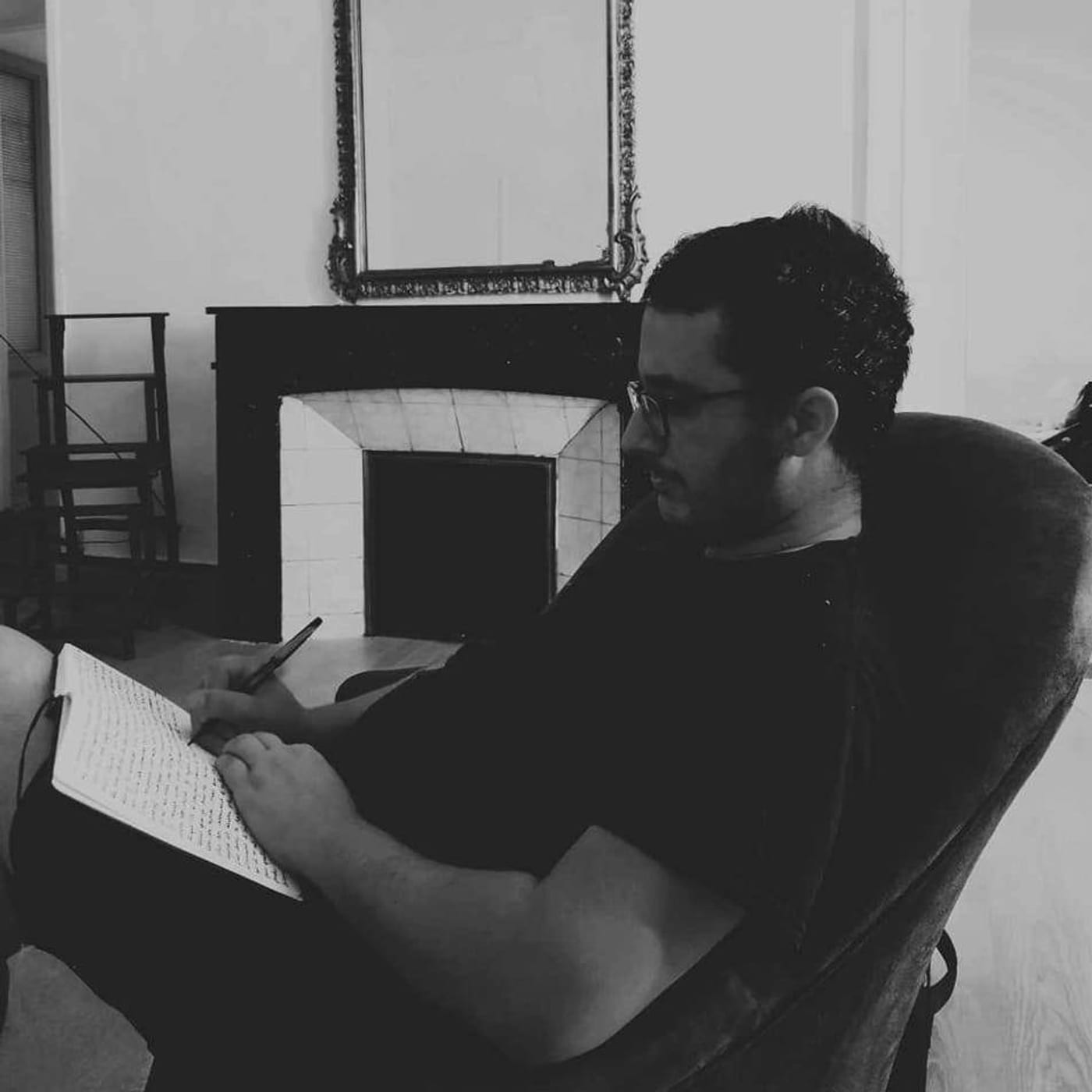 Mathieu Aleins à l'écriture, carnet en main, devant une cheminée ancienne
